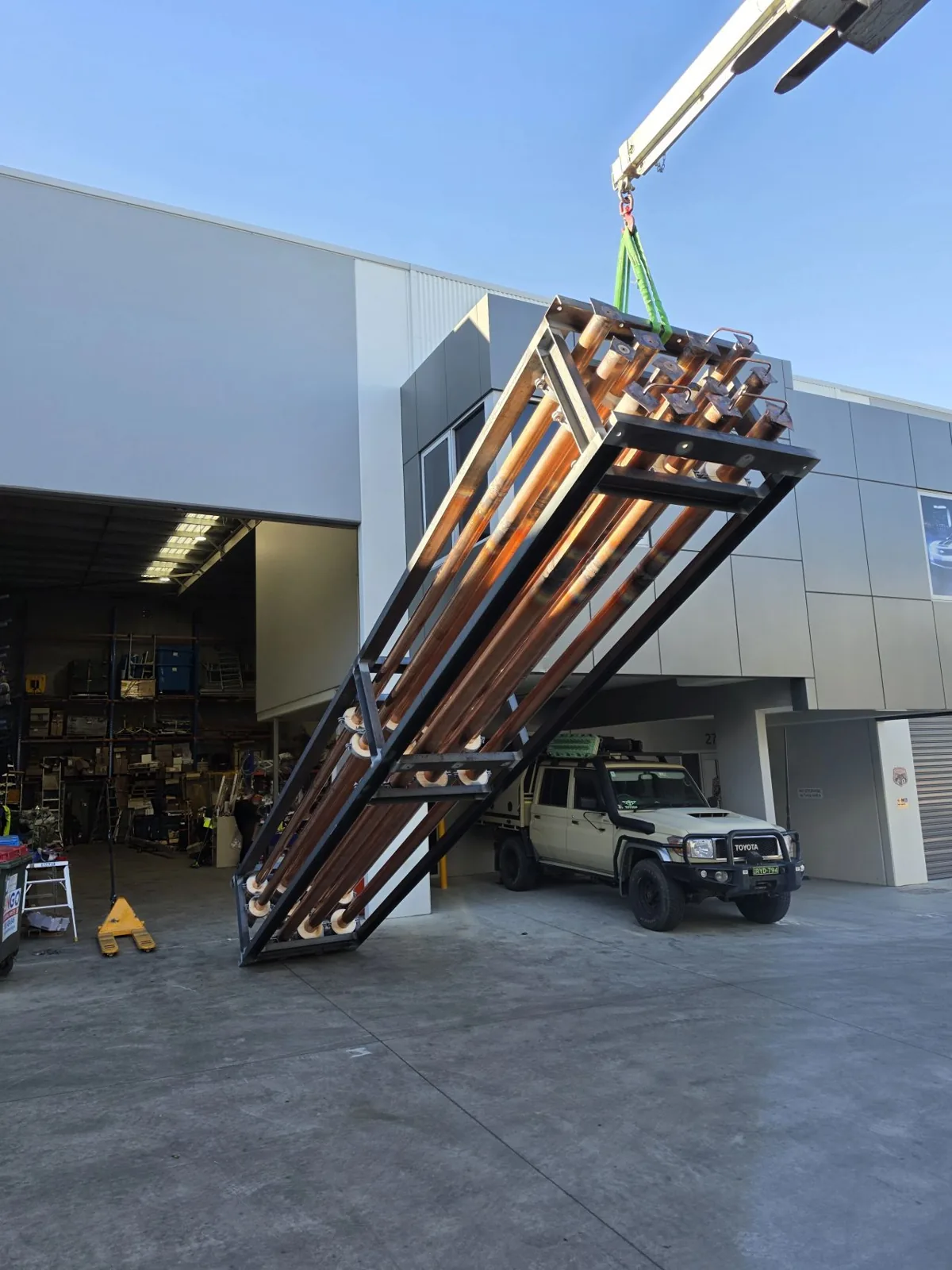 Prefabricated pipework module suspended from a crane outside an industrial workshop